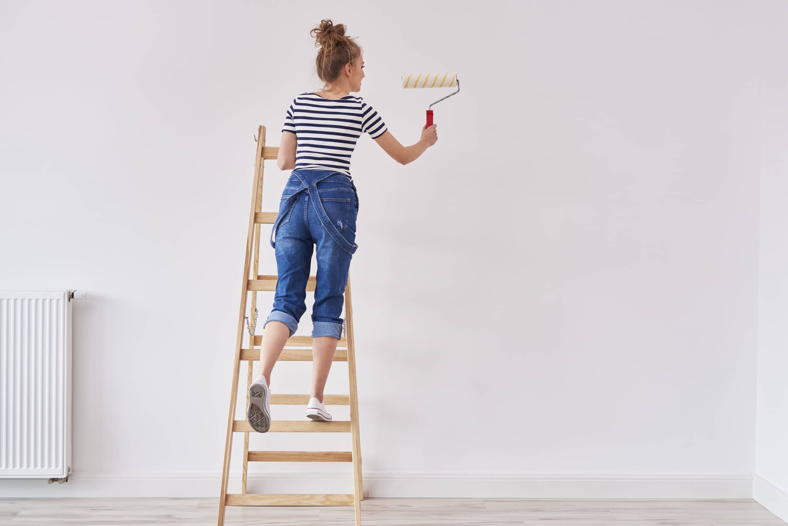 pot de peindre sur une échelle avec une Contexte de une permanent femme  habillé dans salopette et rayé chemisier, vu de derrière, La peinture une blanc  mur avec une rouleau avec bleu peindre 23425583 Photo de stock chez Vecteezy